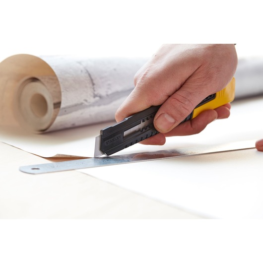 STANLEY 0-10-151 utility knife cutting wallpaper with ruler, close-up photo, hand holding tool.