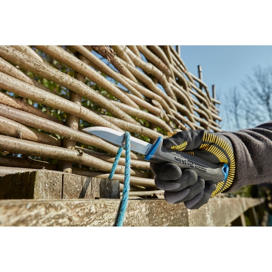 Photo of STANLEY 0-10-232 utility knife cutting blue rope outdoors, product held with gloved hand.