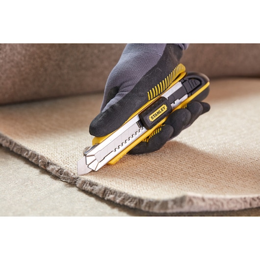 Stanley 0-10-481 utility knife used to cut carpet, close-up of yellow and black tool in hand.