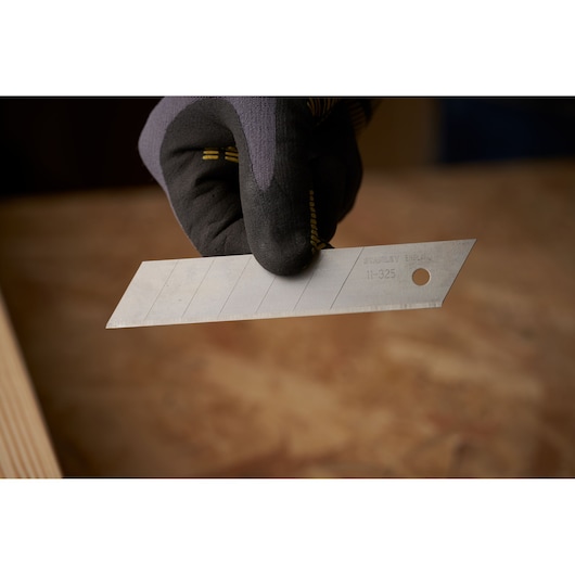 Photo of STANLEY 0-11-325 utility knife blade held by gloved hand, with visible segment lines.