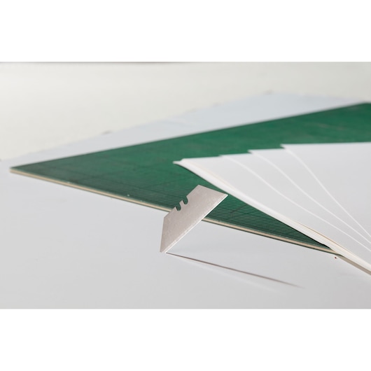 STANLEY 0-11-700 utility blade close-up with green cutting mat and white sheets in background.