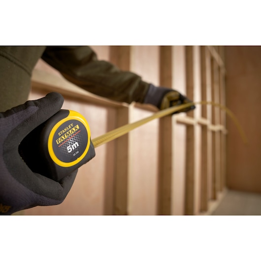 Photo of STANLEY 0-33-720 tape measure, yellow and black, being used to measure wood framing.