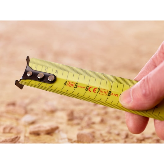 Photo of STANLEY 0-33-720 tape measure with yellow blade, held outdoors, showing metric markings.