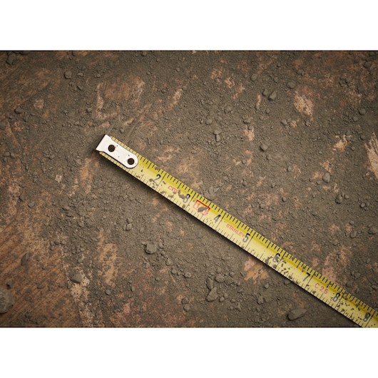 STANLEY 0-39-055 tape measure on rough dusty ground, close-up side angle, yellow ruler with black markings.