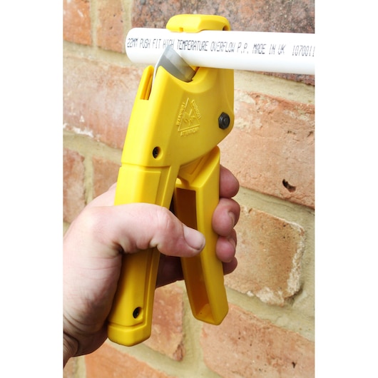 STANLEY 0-70-450 yellow plastic pipe cutter held in hand, cutting white pipe, close-up view.