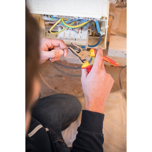 Photo of STANLEY 0-84-001 pliers being used to cut wire during electrical work near a fuse box.