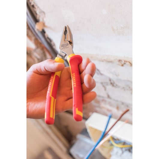 STANLEY 0-84-001 insulated pliers with red and yellow handles, held in hand near exposed wiring.