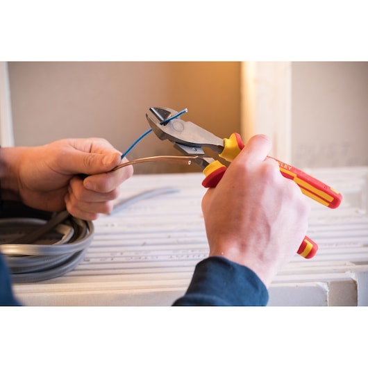 Stanley 0-84-004 insulated diagonal pliers cutting blue wire, close-up photo of hands in workshop.