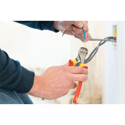Photo of STANLEY 0-84-016 insulated pliers cutting electrical wire near outlet, close-up view.