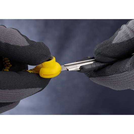 Photo of STANLEY 1-10-409 utility knife cutting yellow plastic, held by gloved hands, close-up.