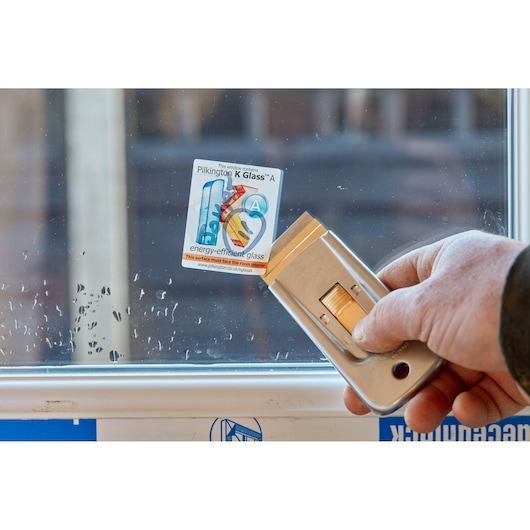 STANLEY 1-11-515 utility blade scraper in hand removing sticker from glass window, close-up angle.