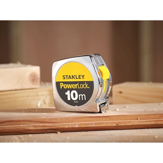 STANLEY 1-33-442 PowerLock 10m tape measure with yellow button on wood surface, side angle.