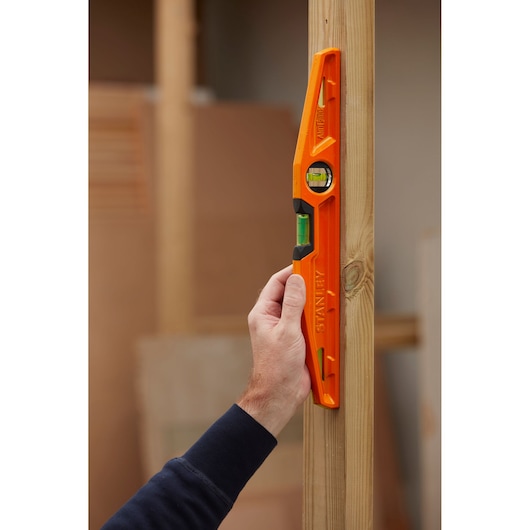 STANLEY 1-42-312 orange spirit level held vertically against wooden beam, photography.