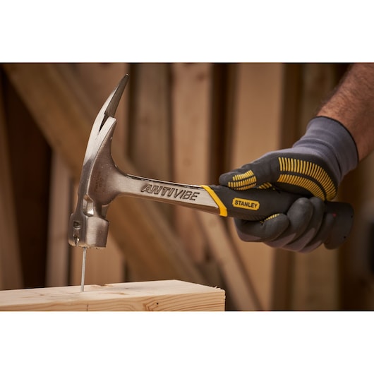 Stanley 1-51-937 claw hammer in use, driving a nail into wood, side angle photo.
