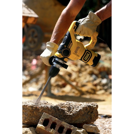 STANLEY FME1250K rotary hammer in use, yellow and black design, drilling into concrete at construction site.