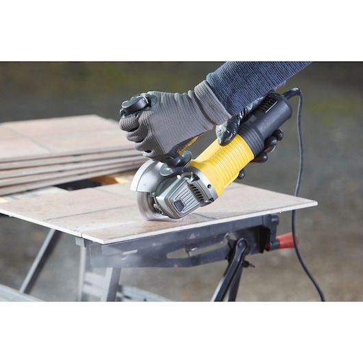 STANLEY FMEG210 angle grinder cutting tiles, close-up photo of tool in use, photography product category.