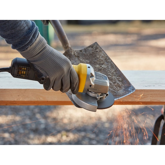 STANLEY FMEG220K angle grinder in use grinding a shovel blade, close-up with sparks flying.