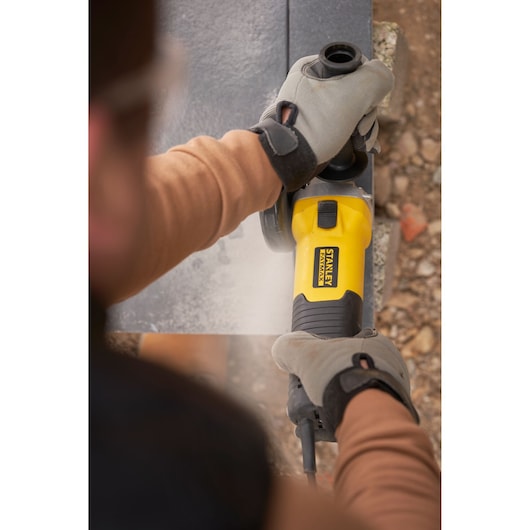 Photo of STANLEY FMEG225VS angle grinder used on stone by gloved hands outdoors.
