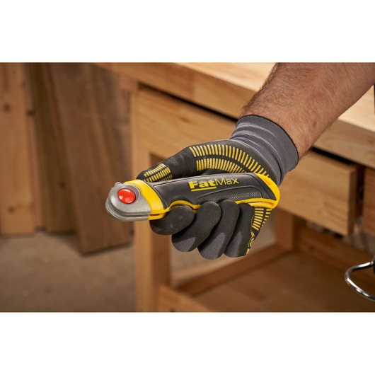 STANLEY FMHT0-20559 FatMax utility knife held in gloved hand, yellow and black handle, workshop background.