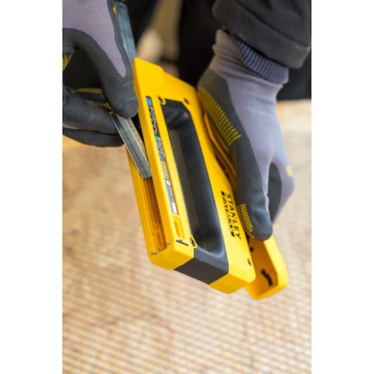 Photo of STANLEY FMHT0-80551 staple gun being loaded, held by gloved hands, close-up view.