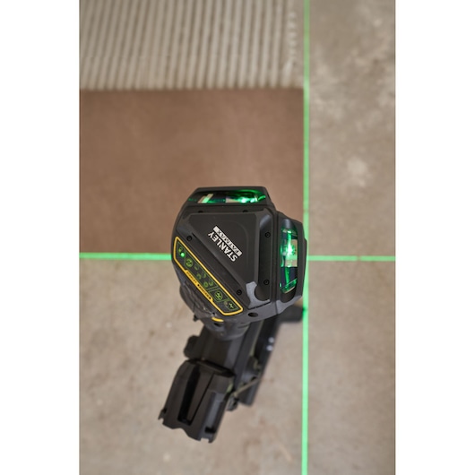 STANLEY FMHT1-77356 laser level projecting bright green lines onto a tiled floor, top view.