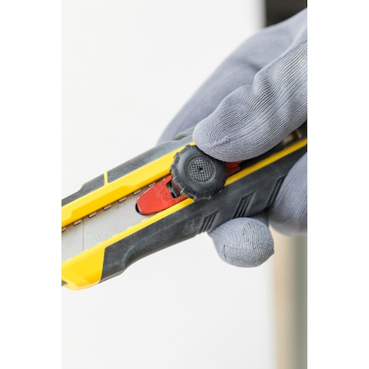 Photo of STANLEY FMHT10330-0 utility knife held in a gloved hand, side view showing blade and adjustment wheel.