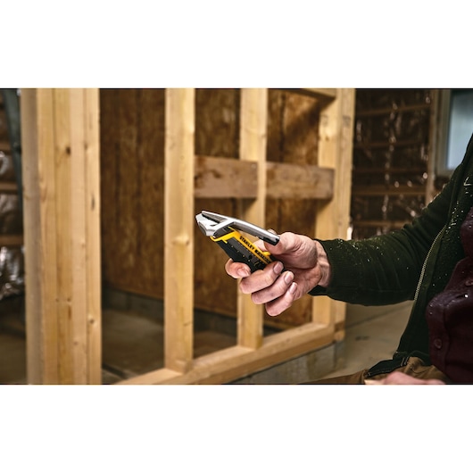 STANLEY FMHT10592-0 utility knife held in hand at construction site, yellow and black handle visible.