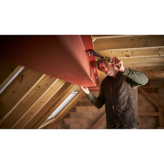 STANLEY FMHT13125-0 pliers used to grip metal beam in attic construction setting, side angle.