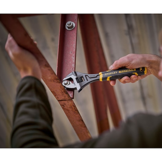 STANLEY FMHT13126-0 adjustable wrench in use tightening a bolt on a red metal frame, close-up photo.
