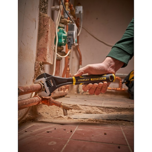 STANLEY FMHT13126-0 adjustable wrench being used on copper pipes in a construction setting.