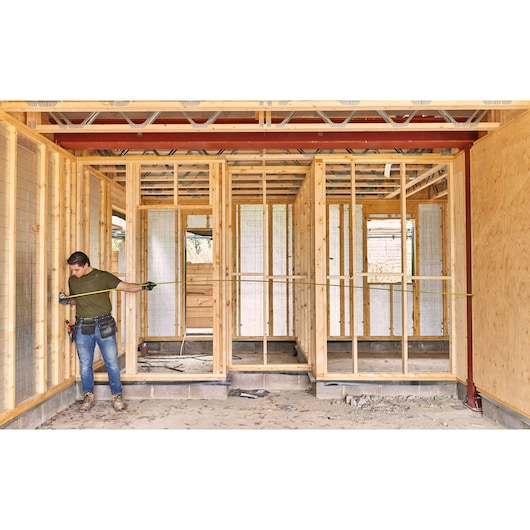 STANLEY FMHT38214-0 tape measure in use at construction site, worker measuring wooden frame.