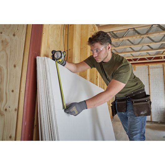STANLEY FMHT38217-0 tape measure in use, measuring drywall panel in construction setting.