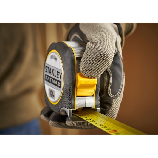 STANLEY FMHT38232-0 tape measure held in gloved hand, close-up, yellow and black design.