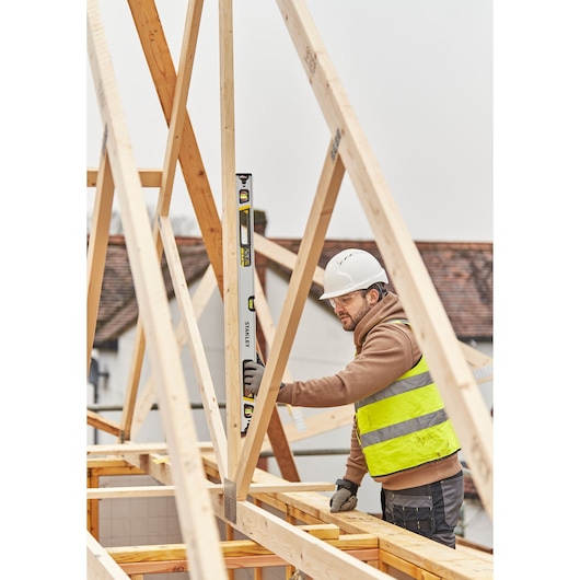 STANLEY FMHT43674-1 spirit level used by construction worker aligning a wooden beam at a building site.