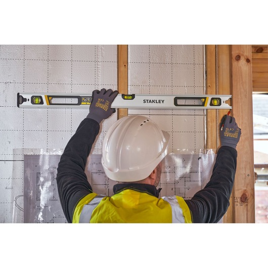 Photo of a worker using STANLEY FMHT43675-1 spirit level on wall, construction site background, product in use.