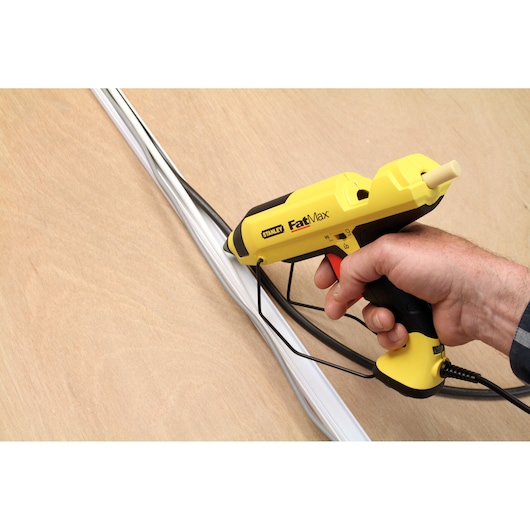 Stanley FMHT6-70418 glue gun held in hand, yellow and black, applying adhesive to wires on wood surface.