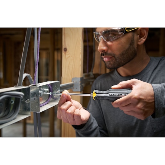 Person uses a STANLEY screwdriver to fasten a screw in an electrical metal box during construction.
