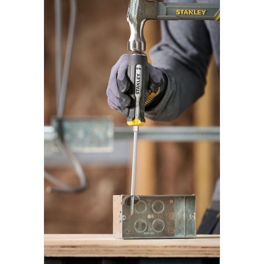 Stanley screwdriver and hammer used to work on a metal electrical box on a wooden surface.