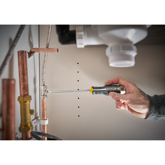 Hand using a STANLEY screwdriver to tighten a pipe clamp under a sink.