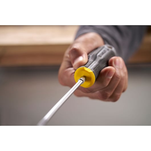 Hand holding a STANLEY screwdriver with a yellow and black handle, photographed close-up.