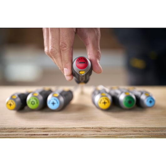 Hand selecting a colored STANLEY screwdriver from a set, arranged on a wooden surface.