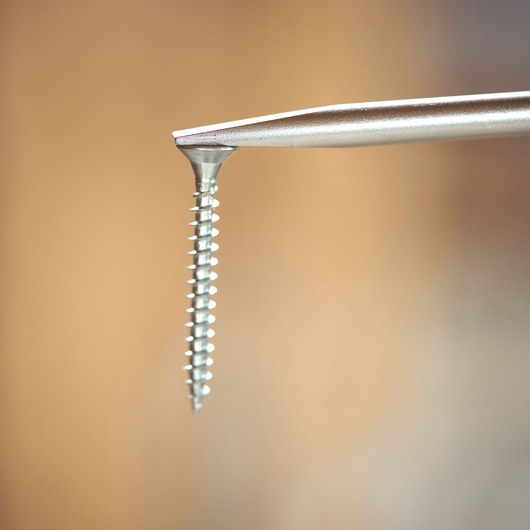 Close-up of a screwdriver tip engaging a metal screw against a blurred background.