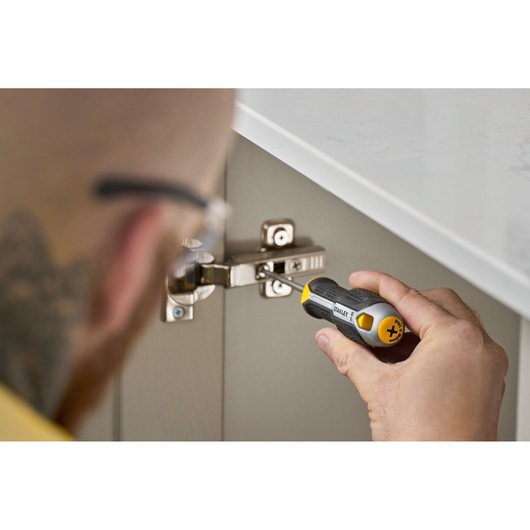 Person uses a STANLEY screwdriver to tighten a screw on a cabinet hinge under a countertop.