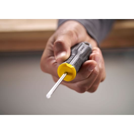 Hand holding a Stanley screwdriver with a yellow handle, shown in close-up against a blurred background.