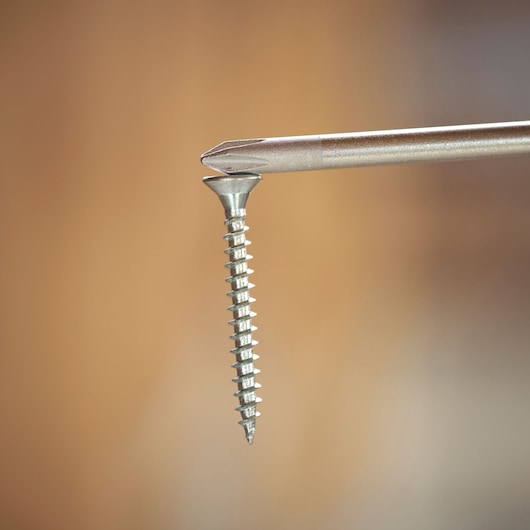 Close-up of a screwdriver tip inserted into the head of a metal screw against a blurred brown background.