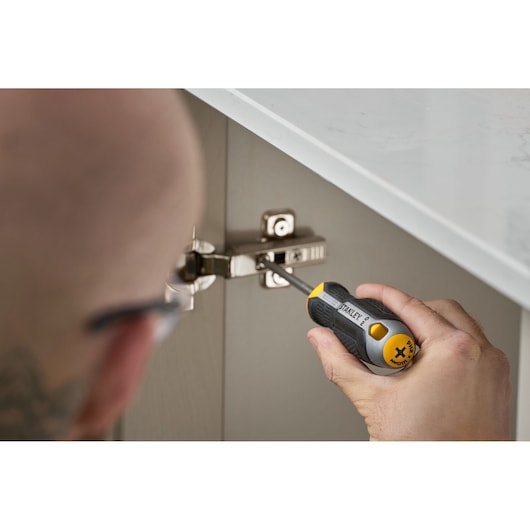 Person uses a Stanley screwdriver to adjust a cabinet hinge beneath a countertop.