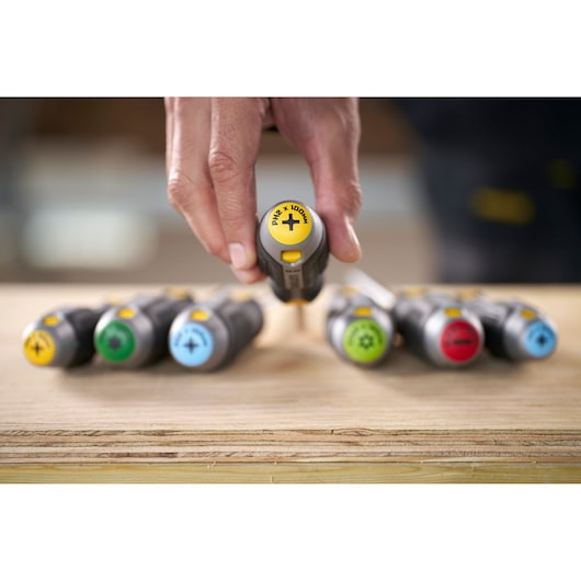 Hand picking a Stanley screwdriver from a set with colored handles on a wooden surface.