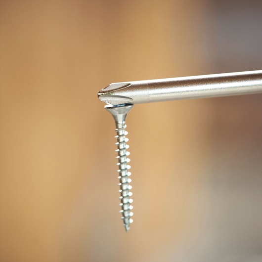 Close-up of a screwdriver tip holding a metal screw against a blurred background.