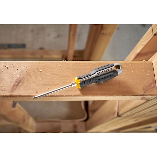 Stanley screwdriver with black and yellow handle on wooden beam in a construction setting.