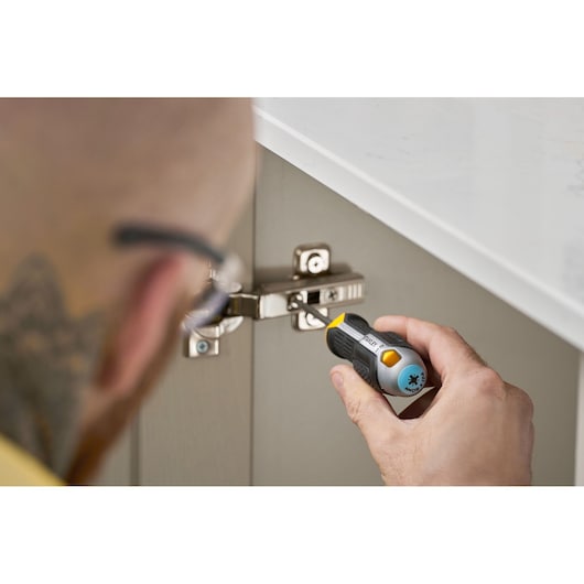 Person uses a STANLEY screwdriver to tighten screws on a metal cabinet hinge under a white countertop.